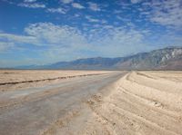 a deserted road in the desert with mountains in the background and water flowing through it