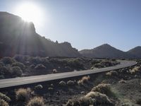 the road goes through a deserted rocky plain into a desert landscape with a mountain in the background