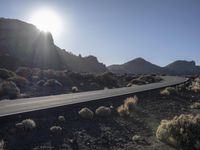 the road goes through a deserted rocky plain into a desert landscape with a mountain in the background