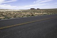 an empty road stretches along a vast open landscaped area, in a deserted region with sparse grass and tall dry brush