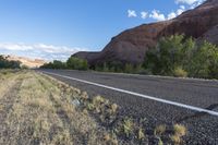 this is an empty road next to a mountain side with a few vegetation and trees in front