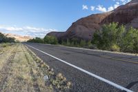 this is an empty road next to a mountain side with a few vegetation and trees in front