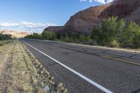 this is an empty road next to a mountain side with a few vegetation and trees in front