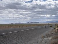 a deserted road in the desert with a mountain in the distance and a few clouds