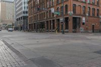 two men walk across a deserted city sidewalk with buildings and a red traffic light on the corner