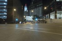 a street is deserted in front of large buildings at night as traffic moves along it