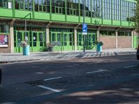 there is a green building on the street corner with cars parked along it and people walking near by