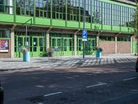 there is a green building on the street corner with cars parked along it and people walking near by