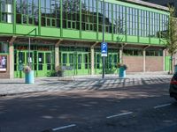 there is a green building on the street corner with cars parked along it and people walking near by