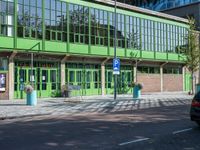 there is a green building on the street corner with cars parked along it and people walking near by