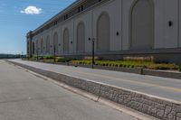 a small road runs along side a large building with columns and arches on the wall