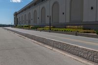 a small road runs along side a large building with columns and arches on the wall