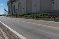 a small road runs along side a large building with columns and arches on the wall