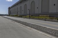 a small road runs along side a large building with columns and arches on the wall