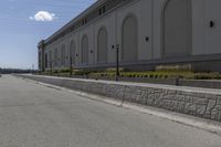 a small road runs along side a large building with columns and arches on the wall