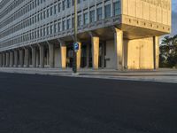 street view of a large concrete building with columns on the sides of it and a parking meter in the middle