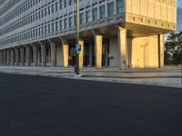 street view of a large concrete building with columns on the sides of it and a parking meter in the middle