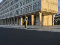 street view of a large concrete building with columns on the sides of it and a parking meter in the middle