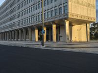 street view of a large concrete building with columns on the sides of it and a parking meter in the middle