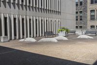 some benches sit on top of concrete pillars by a building that has windows, and plants in them