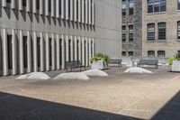 some benches sit on top of concrete pillars by a building that has windows, and plants in them