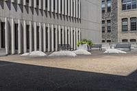 some benches sit on top of concrete pillars by a building that has windows, and plants in them