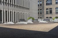 some benches sit on top of concrete pillars by a building that has windows, and plants in them