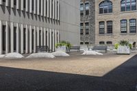 some benches sit on top of concrete pillars by a building that has windows, and plants in them