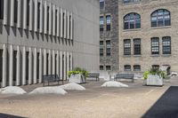 some benches sit on top of concrete pillars by a building that has windows, and plants in them