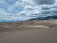 this is an image of a barren desert landscape with mountains in the background and clouds above