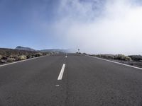 a road near the mountain side in the foggy sun day, and on the opposite bank are hills