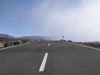 a road near the mountain side in the foggy sun day, and on the opposite bank are hills