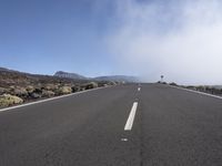 a road near the mountain side in the foggy sun day, and on the opposite bank are hills