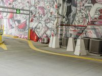 a painted wall in a parking garage next to yellow cones and a blue pole, which are holding a green traffic light