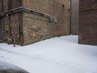 a snow covered sidewalk leading up to an old brick building with exposed windows and pipe work