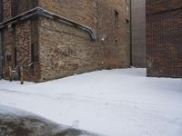 a snow covered sidewalk leading up to an old brick building with exposed windows and pipe work