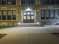 the large brown wooden door is illuminated by lights on the side of a brick building