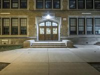 the large brown wooden door is illuminated by lights on the side of a brick building
