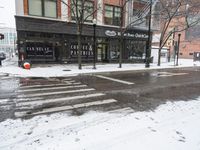 snow covers the streets near a large city building in winter time and pedestrian crossing signs