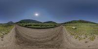 a dirt bike jump on an empty road with mountains in the back ground and green fields in the distance