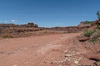 dirt road leading through an arid and rocky desert plain to a cliff in the distance