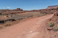 dirt road leading through an arid and rocky desert plain to a cliff in the distance