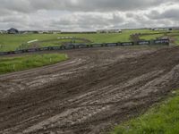 two dirt motocross racers riding a muddy track through a grassy field on cloudy day