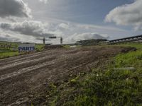 two dirt motocross racers riding a muddy track through a grassy field on cloudy day