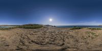 a panoramic photo of a dirt path leading to the beach under a blue sky with a sun behind it