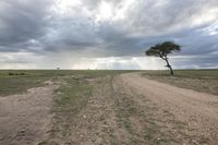 a dirt road running through a vast expanse in the middle of a plain with dark and cloudy skies