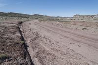 dirt road at badlands area with rocky formation and blue sky in background under bright blue skies