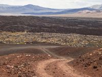 a dirt road that is winding through the barren area of land below mountain ranges and large rocks