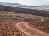 a dirt road that is winding through the barren area of land below mountain ranges and large rocks