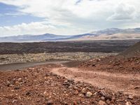 a dirt road that is winding through the barren area of land below mountain ranges and large rocks